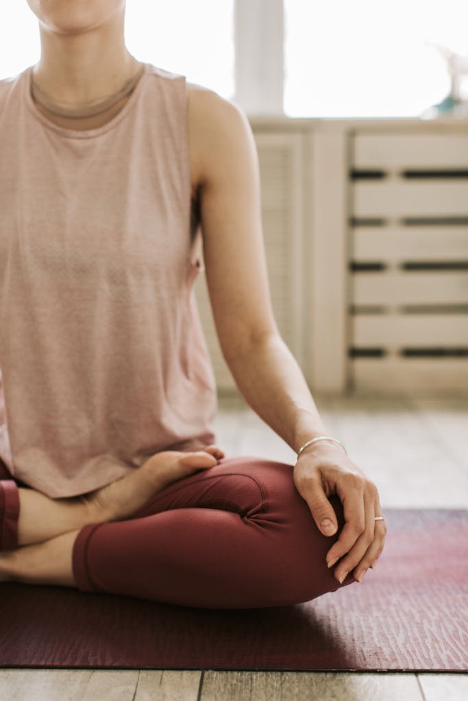 A woman practices meditation in an asana pose on a yoga mat indoors, promoting relaxation and wellness.