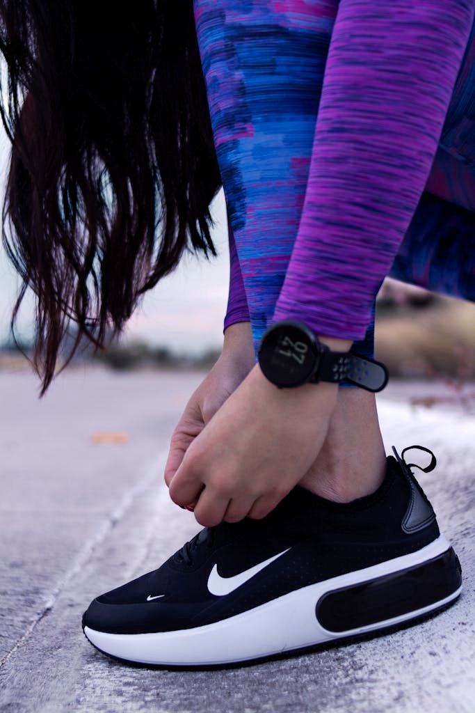 Close-up of a woman tying her sneakers while wearing colorful workout leggings outdoors.